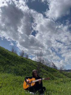 a woman sitting in the grass with an acoustic guitar on her lap and looking up into the sky