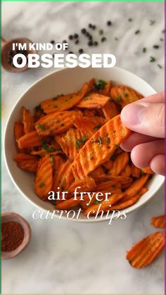 a hand holding a piece of air fryer carrot chips in a bowl with the words i'm kind of obsessed above it