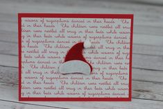 a red and white christmas card with a santa hat on it's head, sitting on top of a wooden table