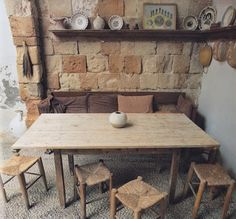 a wooden table and chairs in front of a brick wall with shelves on it, next to a couch