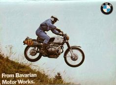 a man riding on the back of a motorcycle in the air over a grass covered hill