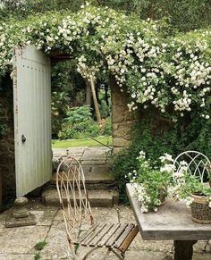 an outdoor table and chairs with flowers growing on the wall next to it in front of a door