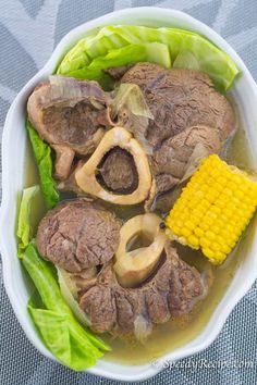 a bowl filled with meat and vegetables next to a corn on top of lettuce