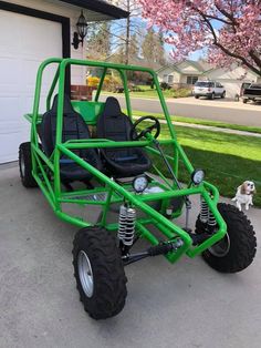 a green go kart parked in front of a garage with a dog standing next to it