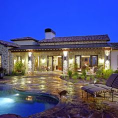 a house with a swimming pool and patio furniture in front of it at night time