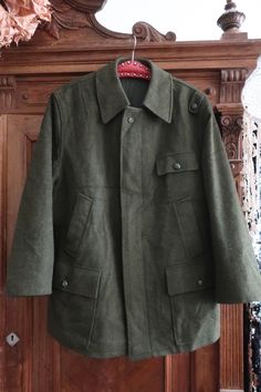 Beautiful True Vintage Austrian wool coat from traditional Tyrolean trachten brand Pischl. Made of high quality heavy loden boiled wool in a beautiful green color tone. Diamond quilted lining. Large collar. Hidden button tab, football button details. Some utility features and asymmetric details, incl. two side pockets, two flap pockets, one breast pocket and one inner pocket. Adjusters on the waist. Decorative stitching on the right shoulder, the left shoulder with football button detail. Elastic cuffs in the inner sleeves as wind stoppers. Made in Austria! We like the asymmetric details and utility features - the coat looks great with a pair of corduroy trousers and a rollneck jumper! ERA: 1980s BRAND: Pischl Original Tyroler Loden COLOR: Dark green FABRIC: 95% wool, 5% polyamide; synthet Khaki Wool Outerwear With Buttons, Green Tweed Jacket With Button Closure For Winter, Classic Green Wool Coat, Vintage Olive Outerwear With Buttons, Green Wool Outerwear With Buttons, Vintage Wool Outerwear With Buttons, Military Style Wool Outerwear In Khaki, Vintage Khaki Wool Outerwear, 1980s Mens Fashion