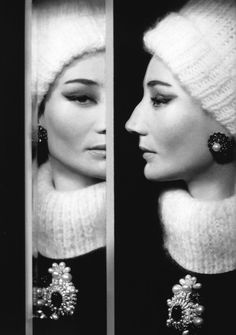 a woman wearing earrings and a knitted hat looks in the mirror to her left