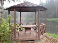 a wooden gazebo sitting on top of a lush green field next to a lake