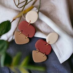 two tone leather heart shaped earrings on top of a white cloth next to a plant