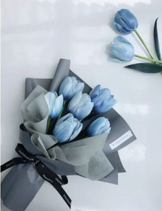 a bouquet of blue tulips tied to a gray ribbon on a white surface