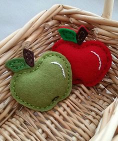 two felt apples sitting in a basket on top of wicker flooring, one green and the other red