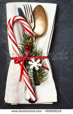 christmas table setting with silverware, candy canes and pine cones on white napkin