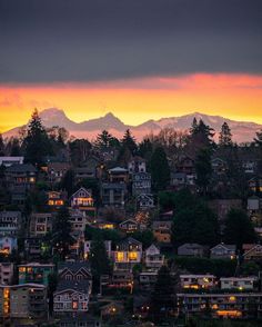 the sun is setting over a city with mountains in the backgrouund and houses on the hillside