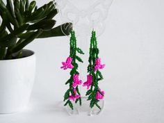 pink and green beaded flowers are hanging from clear acrylic stands next to a potted plant