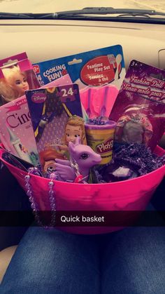 a pink basket filled with barbie dolls and other items sitting on top of a car seat