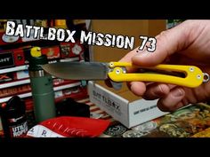 a hand holding a yellow knife in front of a store shelf filled with boxes and other items