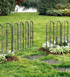 two iron garden gates in the middle of a grassy area with flowers and shrubs around them