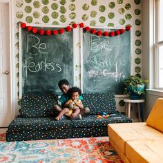 two children sitting on a couch in front of chalkboard wall with writing on it