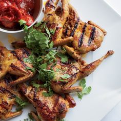 grilled chicken legs with garnishes and sauce on a white platter