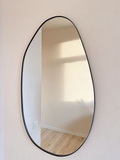 an oval mirror hanging on the wall next to a wooden floor in a white room