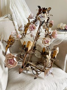 an arrangement of flowers and candles on a couch in a room with white linens