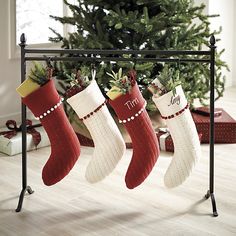 three stockings hanging from a rail with presents underneath it and a christmas tree in the background