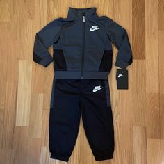 Adorable Nwt Nike Track Suit, Size 24 Months. Full Zip Jacket With Functional Side Slant Pockets 100% Nylon Jacket Is Charcoal Gray With Black Nike Logo On Chest And On Joggers Elasticized Waist And Bottom Cuffs Black Winter Sports Sets, Nike Long Sleeve Sports Sets, Nike Gray Cotton Outerwear, Gray Sportswear Set For Sports, Gray Long Sleeve Playwear Sets, Sporty Black Sets For Fall, Nike Sporty Sets For Playtime, Black Playwear Sets For Fall, Black Sets For Playwear In Fall