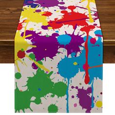 a table covered with colorful paint splattered on it's sides and a wooden surface in the background