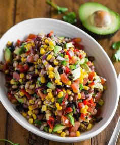 a white bowl filled with corn salad next to an avocado on the side