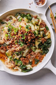 a white bowl filled with noodles and vegetables next to chopsticks on a table