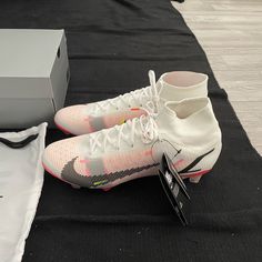 a pair of white and pink shoes sitting on top of a black mat next to a box