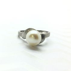 This vintage ring features a 8mm round cultured pearl, creamy white with a beautiful high lustre all set in 10 karat white gold. Curled around the pearl are two 10 karat white gold leaves in a brushed texture. Please message me if you have any questions. Thank you for looking! Metal: 10 karat white gold  Gemstone: Cultured Pearl  Period: 1960's Total weight: 2.77 grams  Markings: 14k (tested lower) Size: 7  Unless stated otherwise, all the items we sell are pre-owned/pre-loved. It is normal for Silver Akoya Pearl Ring For Anniversary, White Gold Pearl Ring For Anniversary, Modern Round Pearl Rings, Silver Akoya Pearl Drop Ring, Classic White Pearl Ring For Gifts, Modern White Pearl Ring For Anniversary, Formal Silver Pearl Drop Ring, Minimalist Formal Round Pearl Ring, Formal Minimalist Round Pearl Ring