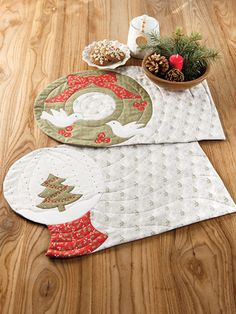 two quilted placemats sitting on top of a wooden floor next to a potted plant