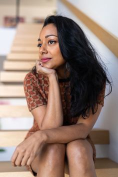 a woman is sitting on the stairs with her hand under her chin