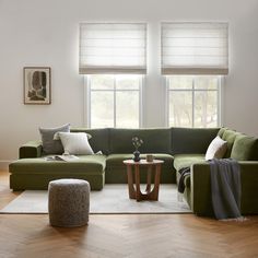 a living room with green couches and pillows on top of the floor, next to two windows