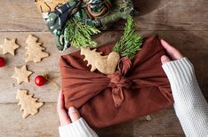 a person holding a wrapped present in front of christmas cookies and other holiday decorations on a wooden table