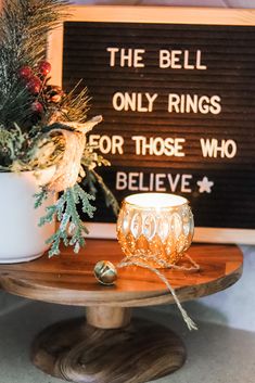 a wooden table topped with a white vase filled with flowers next to a sign that says the bell only rings for those who believe