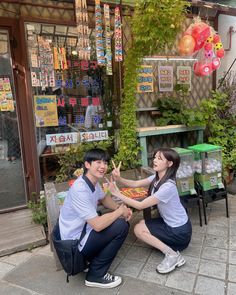 two young people sitting on the ground in front of a store giving each other high five fingers