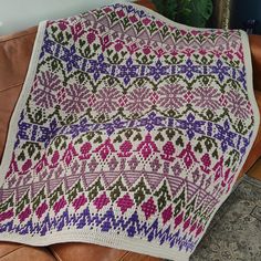 a crocheted blanket sitting on top of a brown leather couch next to a potted plant