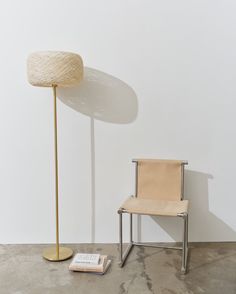 a chair next to a lamp and a book on the floor in front of a white wall