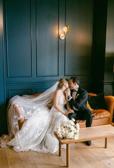 a bride and groom sitting on a couch in a room with dark blue paneled walls