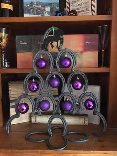 a metal christmas tree with purple ornaments on it's stand in front of a bookshelf