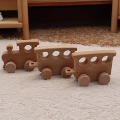 three wooden toy trains sitting on top of a white rug in front of a chair