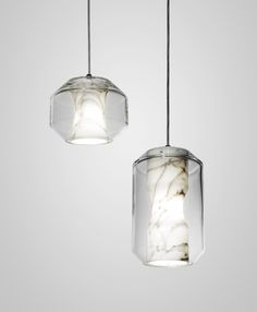 two glass pendant lights hanging from a ceiling fixture with marbled material and metal wires