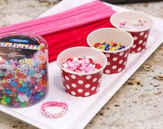 three cups filled with colorful beads on top of a white tray next to a pink ribbon