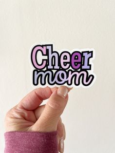 a hand holding up a sticker that says cheer mom