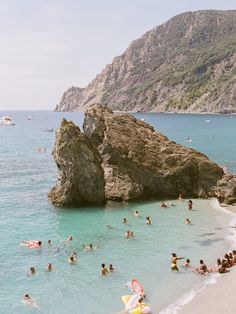 many people are swimming in the ocean near large rocks