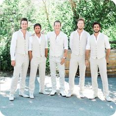 four men in white tuxedos are posing for a photo with wine barrels behind them