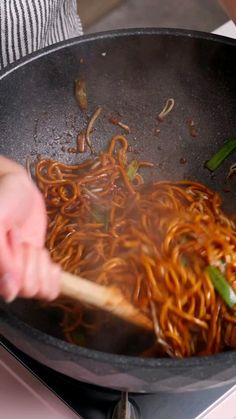 someone cooking noodles in a wok on the stove