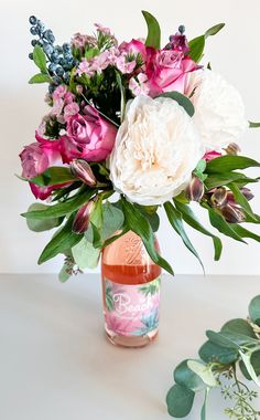 a vase filled with lots of flowers sitting on top of a table next to a plant